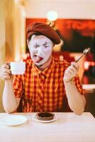 de clown är äter en kaka i en Kafé och hans ansikte är kväkande. foto