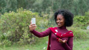 afro flicka talande till henne social media följare i en leva berg leva på en berg klädd i röd. foto
