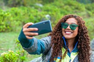 Söt latina och turism vlogger med grön glasögon och lockigt hår som visar henne följare de berg plats var hon är. foto