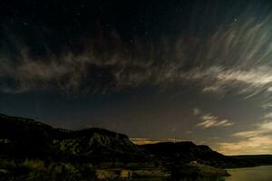 de natt himmel över en sjö med moln och stjärnor foto
