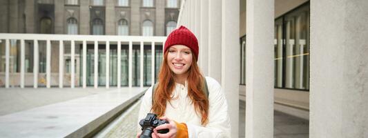 skön läshuvud flicka, fotograf med professionell kamera tar bilder utomhus, gående runt om stad och tar foton, sightseeing foto