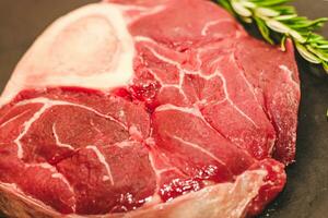 färsk bit av kött stor nötkött biff på de ben ossobuco med en kvist av rosmarin på en svart bakgrund foto