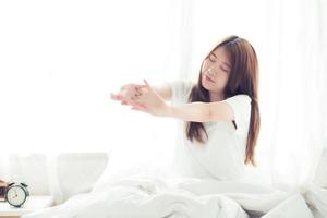 ung asiatisk kvinna stretch och slappna av i sängen efter att ha vaknat på morgonen. foto