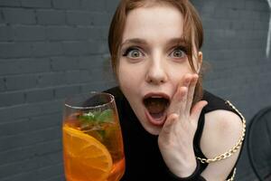 porträtt av en skön roligt Wow uttryck ung kvinna med en glas av cocktail foto