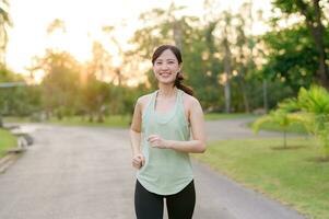 passa asiatisk ung kvinna joggning i parkera leende Lycklig löpning och njuter en friska utomhus- livsstil. kvinna joggare. kondition löpare flicka i offentlig parkera. friska livsstil och wellness varelse begrepp foto