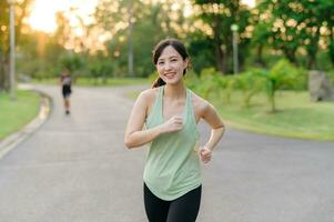 passa asiatisk ung kvinna joggning i parkera leende Lycklig löpning och njuter en friska utomhus- livsstil. kvinna joggare. kondition löpare flicka i offentlig parkera. friska livsstil och wellness varelse begrepp foto