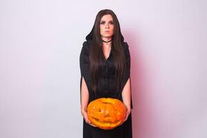 ung kvinna i halloween häxa kostym i studio med gul pumpa. foto