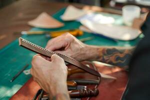 närbild och beskära händer av läder hantverkare är arbetssätt hård till sy en läder produkt för en kund. foto