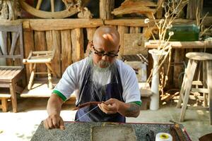 närbild hand av asiatisk läder hantverkare är försiktigt till sy en läder bälte för en kund., läder hantverkare begrepp. foto