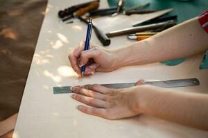 närbild händer av ung kvinna läder varor tillverkare är teckning en design på läder i läder verkstad. foto