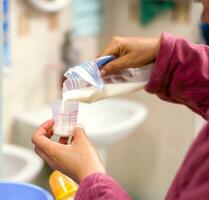 de sjuksköterska händer är häller mors färsk mjölk från de plast väska för mjölk lagring till medicin mätning glas kopp för sjuk nyfödd bebis i de sjukhus. foto