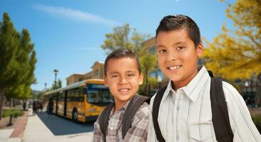 två Lycklig ung latinamerikan Pojkar bär ryggsäckar nära en skola buss på campus foto