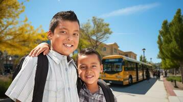 två Lycklig ung latinamerikan bröder bär ryggsäckar nära en skola buss på campus. foto