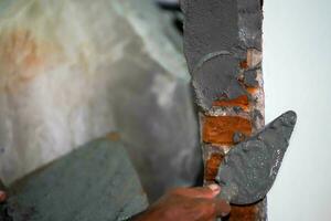 närbild händer av byggare innehav murbruk panorera och putsning väggar med cement i konstruktion webbplats. foto