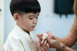 liten asiatisk pojke ger en jasmin krans till mor på thailands nationell mors dag foto