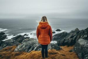 ai genererad en ung kvinna är stående på de kant av en klippa och ser på de hav, kvinna ensam ser på dimmig hav reser äventyr livsstil utomhus- ensamhet ledsen känslor vinter- ner foto