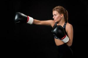skön kvinna idrottare i boxning handskar, i de studio på en svart bakgrund. foto