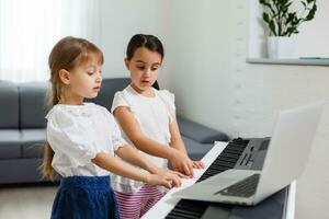 Hem piano lektion. två flickor öva ark musik på ett musikalisk instrument. familj begrepp. de aning av aktiviteter för barn under karantän. foto