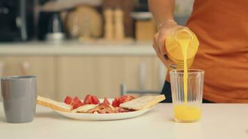 kvinna häller färsk juice i glas för frukost i kök. kvinna dricka friska och naturlig orange juice. hemmafru dricka friska, naturlig, hemlagad orange juice. uppfriskande söndag morgon- foto