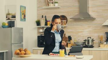 frilansare dricka kaffe i de morgon- på tabell topp under frukost använder sig av läsplatta dator. företag kvinna läsning de sista Nyheter uppkopplad innan gående till arbete, använder sig av modern teknologi i de kök medan äter en friska måltid foto