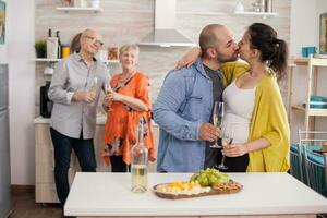 ung man kissing fru i från av hans föräldrar under brunch i kök. blandad ost och vindruvor på trä- platå. foto