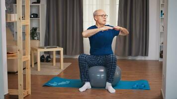 senior man Träning på stabilitet boll i levande rum. gammal person pensionär friska Träning sjukvård sport på Hem, utövar kondition aktivitet på äldre ålder foto