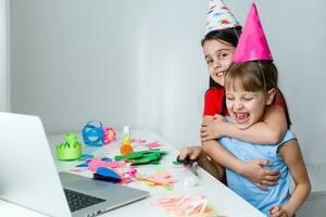 en liten flicka, kurvor och skrattar i främre av en bärbar dator i en keps. firar födelsedag via internet i karantän tid, självisolering och familj värden, uppkopplad födelsedag. Grattis till de animatör foto