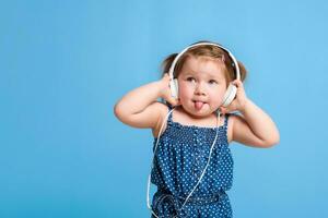 söt liten flicka i hörlurar lyssnande till musik använder sig av en läsplatta och leende på blå bakgrund foto