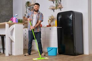 Make hushållerska rengör de kök. ung Lycklig man med grön mopp tvättar de golv foto