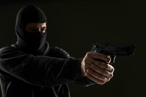 de rånare i en mask med en pistol spetsig till de sida på en svart bakgrund foto