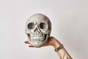 tatuerade hand av en kvinna i en svart Kolla på är innehav en realistisk modell av en mänsklig skalle med tänder isolerat på vit. närbild skott. foto