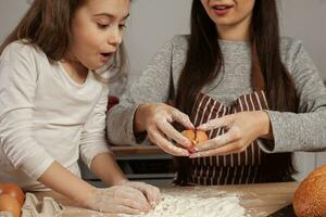 mor och henne dotter är bakning en bröd och har roligt på de kök. foto
