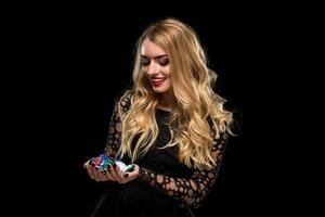 elegant blond i en svart klänning, kasino spelare innehav en näve av pommes frites på svart bakgrund foto