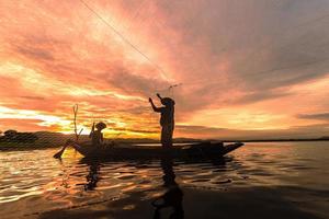 silhuettfiskare som fiskar genom att använda nät på båten på morgonen i thailand, natur- och kulturkoncept