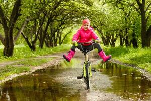 liten flicka ridning cykel i vatten pöl foto