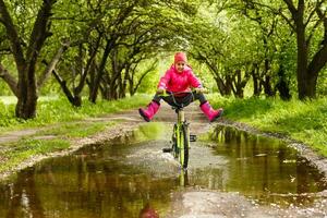 liten flicka ridning cykel i vatten pöl foto