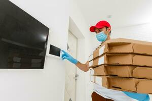 man från leverans service i t-shirt, i skyddande mask och handskar ger mat beställa och innehav pizza lådor över vit bakgrund foto