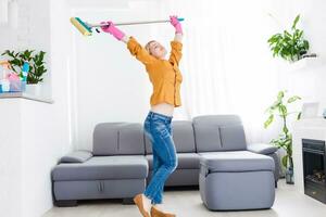 ung kvinna med housecleaning redskap danser i de levande rum. foto