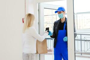 kurir, leverans man i skyddande mask och medicinsk handskar levererar hämtmat mat. leverans service under karantän, sjukdom utbrott, coronavirus covid-19 pandemi betingelser. stanna kvar Hem foto