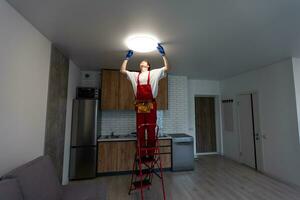elektriker på arbete. service för de reparera av elektrisk ledningar och ersättning av tak lampor. en byggare är montera en loftstil trä- tak. hyresagent hjälper med de hushållsarbete foto