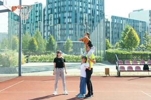 sommar högtider, sport och människor begrepp Lycklig familj med boll spelar på basketboll lekplats foto