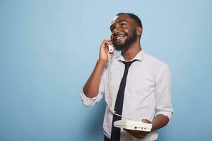 afrikansk amerikan manlig vuxen framställning en telefon ring upp på en fast telefon. leende affärsman på ett analog telefon telefon, chattar bort. en samtida enskild har roligt och tar samtal foto