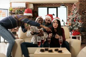 Lycklig medarbetare dricka alkohol och njuter trösta gaming på jul fest i dekorerad kontor. glad kollegor fira ny år vinter- säsong- Semester tillsammans foto