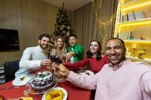 video ring upp för jul, olika vänner talande på en smartphone och tar en selfie gemensam Foto Sammanträde på Hem på de festlig tabell nära de jul träd, ny år högtider.
