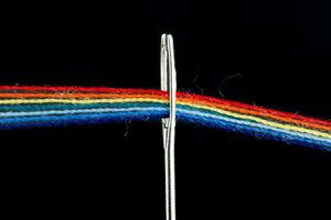 flerfärgad trådar för sömnad i de form av en regnbåge passera genom ett antik nål på en svart bakgrund foto