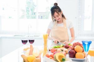kvinna som lagar och skivar grönsaker i köksrummet med full mat och frukt på bordet. semester och lycka koncept foto