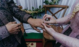 brud sätter en ringa på de brudgum finger. ceremoni och bröllop planera. guld ringar för muslim brudar i Indonesien. engagemang ögonblick. foto