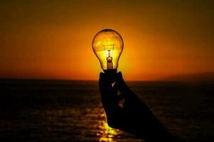 en person innehav upp en ljus Glödlampa över de hav foto
