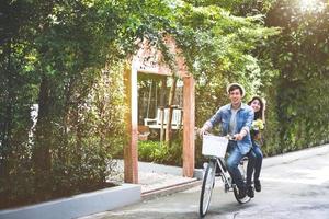 lyckligt par som cyklar tillsammans i romantisk utsikt park bakgrund. alla hjärtans dag och bröllop smekmånad koncept. människor och livsstil koncept