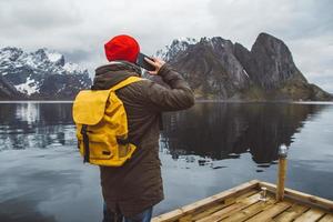 man pratar i mobiltelefon i en gul ryggsäck som står på en bakgrund av ett berg och en sjö foto